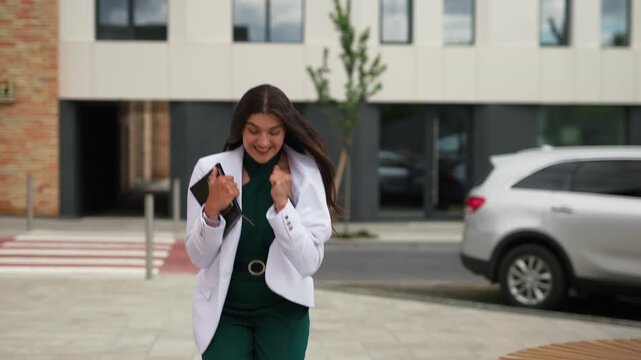 Excited young business woman celebrating success and gesturing yes outdoors, slow motion