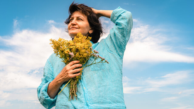 Happy woman holding bouquet of wild yellow flowers, enjoying freedom and summer under a clear blue sky