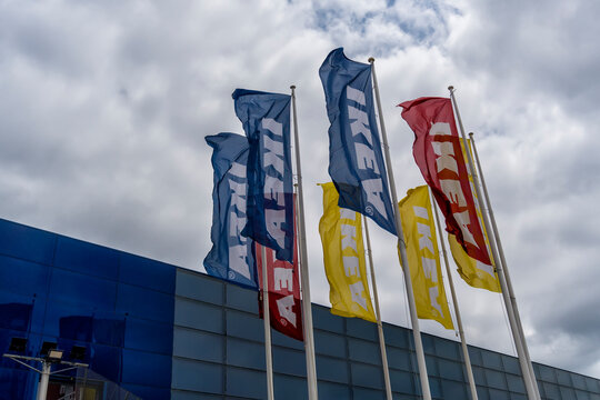 Plano contrapicado de coloridas banderas de IKEA ondeando al viento sobre m&aacute;stiles afuera de un edificio comercial con fachada de cristal contra un espectacular cielo nublado en Barcelona, Espa&ntilde;a.