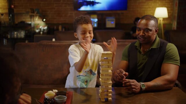 Black father helping son build wooden block tower