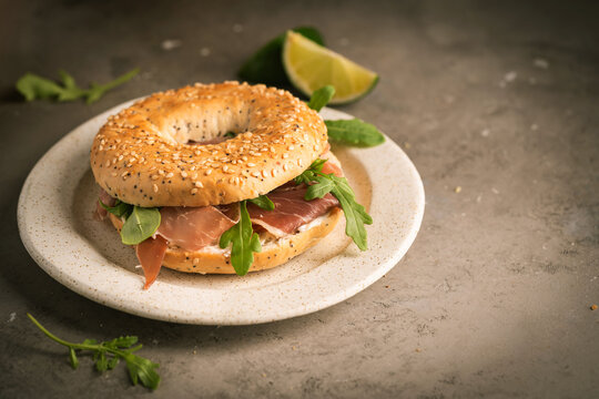 Sandwich with ricotta, prosciutto and microgreens, bagel with ham for breakfast on gray background, close up.