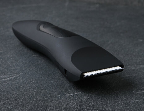 Studio product shot of a minimalist black cordless trimmer. Elegant personal care appliance presented on a textured dark stone background with soft studio light.