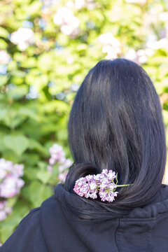 Dark haired girl with lilac flowers on her hair. Rear view.
