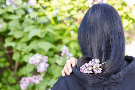 Dark haired girl with lilac flowers on her hair. Rear view. Closeup.