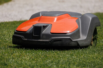 A robotic lawn mower works on green grass in a residential garden. It cuts grass without human help...