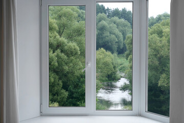 Fototapeta premium A view from the window of a landscape with green willows on the riverbank.