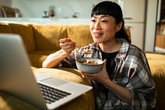 Woman eating breakfast and watching laptop at home