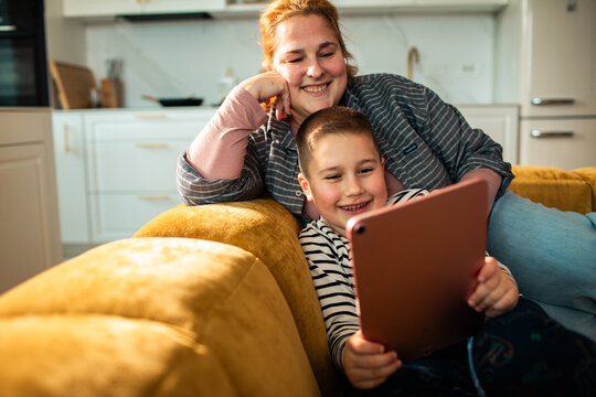 Smiling mom and son using tablet on cozy sofa at home