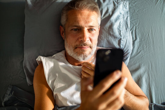 Middle-aged man using smartphone in bed
