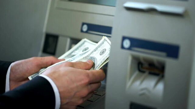 Man counting dollars withdrawn from ATM machine and putting cash in wallet for convenience and 24h banking service in 4K Ultra HD footage
