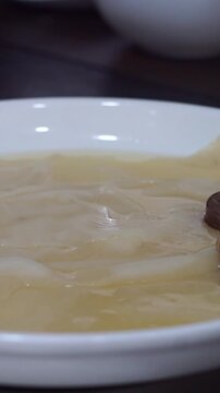 Close up of chef in white gloves arranging sliced boiled beef and kazi horsemeat sausage over dough sheets on a white plate, vertical video.