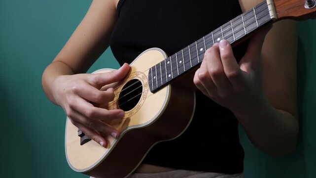 Young woman playing acoustic ukulele against a teal backdrop