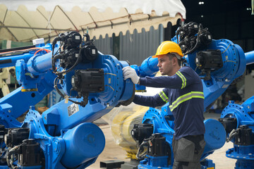 Fototapeta premium Worker in a facility adjusts robotic arm during assembly process at manufacturing site