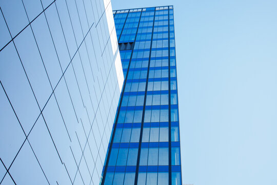 Glass skyscraper building facade exterior with the background of blue sky low angle view. Modern business office building architecture, repetitive contemporary design, big city life.