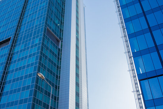 Two glass skyscraper building facades exterior with the background of blue sky low angle view. Modern business office building architecture, repetitive contemporary design, big city life.
