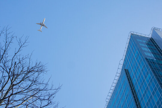 Civil aviation plane flying over the big city downtown with glass office buildings Contemporary background, modern exterior, urban architecture
