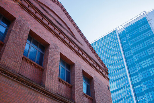 Compound of old style red brick building with modern glass skyscraper on the background. Modern big city design and architecture, restoration of buildings, past and future togetherness concept.