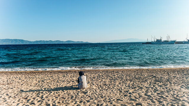 Person Sitting on Nea Roda Beach Facing Fishing Boats