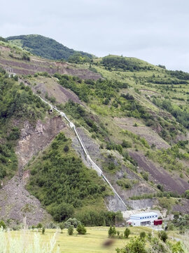 View of an industrial hydroelectric power plant system stretching down a steep, rocky slope covered in lush vegetation in Turkey's Ardahan province, along with a facility at the foot of the slope.