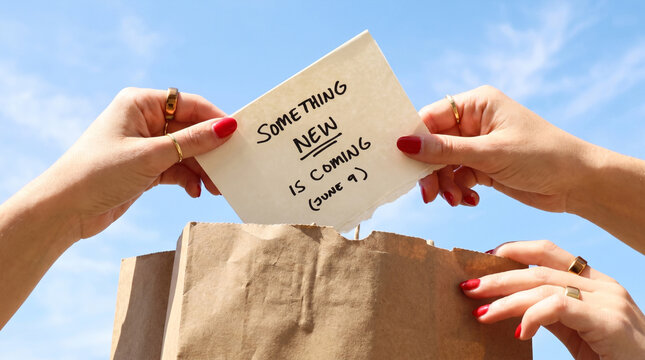 Hands taking out note with Something New Is Coming message from paper bag
