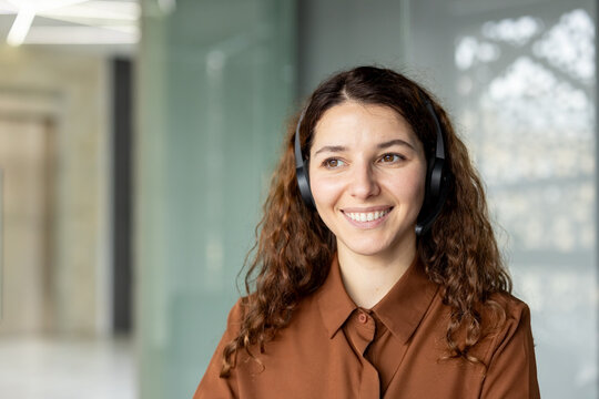 Smiling young woman with curly hair wearing a headset, providing excellent customer service and support, looking positive and professional in a modern office environment