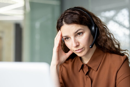 Woman wearing a headset experiencing stress and a headache at her workspace, feeling overwhelmed and frustrated while working in a demanding customer support environment