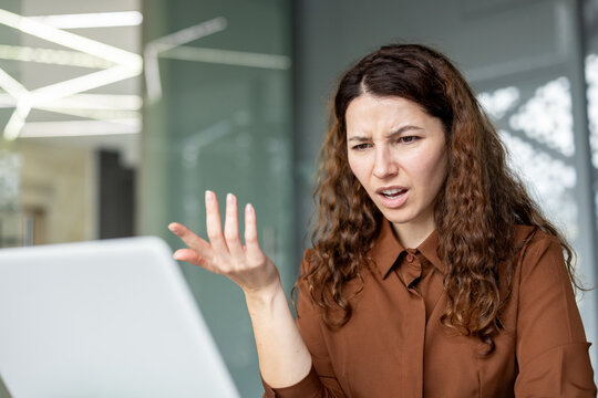Professional woman working in an office setting, looking puzzled and stressed while facing a problem or error on her computer, expressing technology difficulties and disappointment