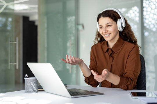 Young business professional communicating during a remote work meeting, gesturing while listening and speaking on a laptop in a modern office environment