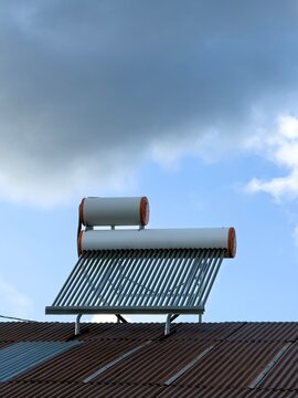 View of a solar water heater mounted on a corrugated metal roof under a cloudy blue sky in Posof, Ardahan, Turkiye.