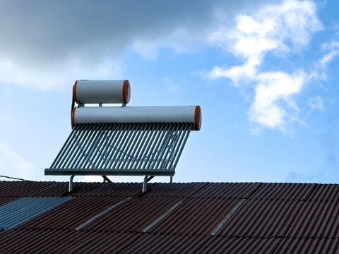 View of a solar water heater mounted on a corrugated metal roof under a bright blue sky with clouds in Posof, Ardahan, Turkiye.