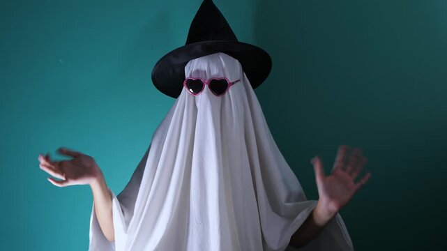 Funny ghost costume with heart sunglasses gesturing on teal backdrop