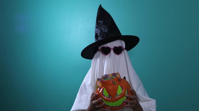 Child in ghost costume holding pumpkin candy pail on Halloween