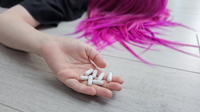 A teenage child commits suicide by overdose on medication. A close-up of the pills and the addict on the floor