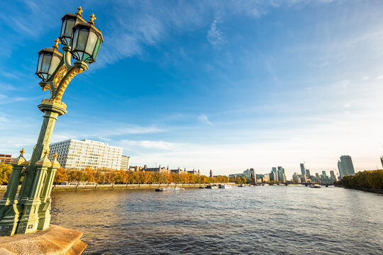 View of the River Thames with an ornate Victorian lamp post in the foreground and the London skyline in the background under a clear blue sky in London, England, United Kingdom.