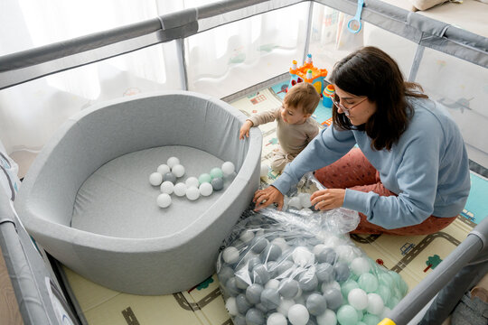 Mother and toddler setting up ball pit in playpen at home
