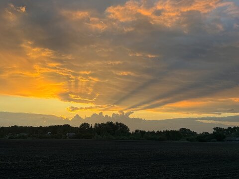 Dramatic golden sunset sky with crepuscular sun rays shining through clouds over dark field