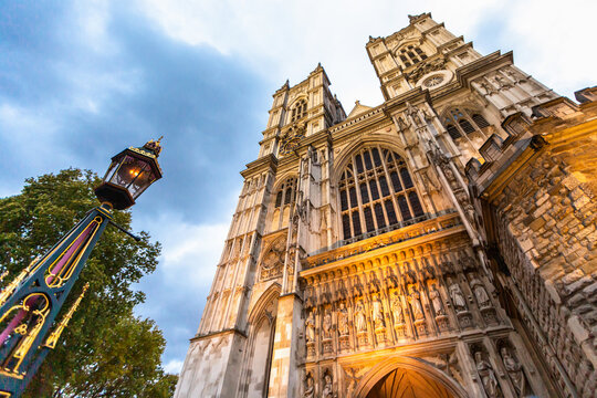 View of Westminster Abbey with its intricate gothic architecture, stone carvings, and a decorative lamp post in the foreground under a cloudy sky in London, England, United Kingdom.