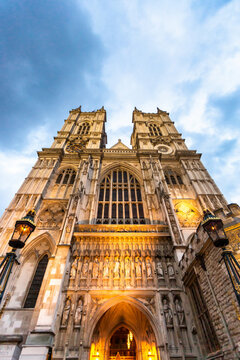 View of the ornate Gothic facade and twin towers of Westminster Abbey illuminated at dusk in London, England, United Kingdom.