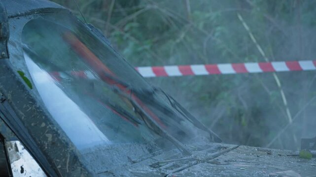 Close-up of dirty off-road car. Wipers clearing mud from windscreen during extreme outdoor rally. Red and white tape in background. Adventurous and rugged scene