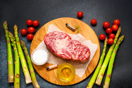 Fresh meat cherry tomatoes and asparagus arranged on a wooden board for cooking preparation