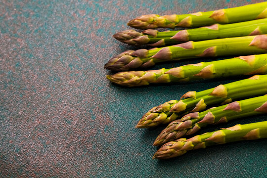 Fresh asparagus arranged on a textured surface with varying green shades during daylight