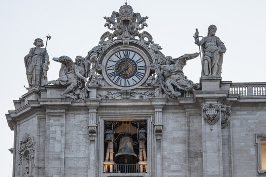 View of the ornate clock and bell tower of St. Peter's Basilica with intricate baroque statues and Roman numerals on the clock face in Rome, Lazio, Italy.