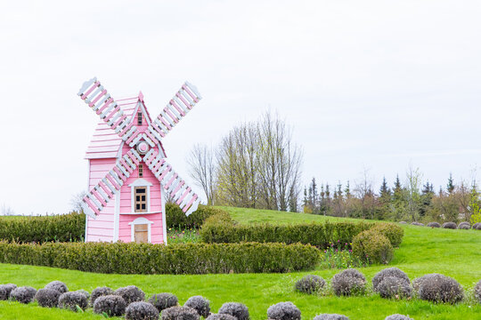 Charming pink windmill stands gracefully in a vibrant green landscape under a cloudy sky