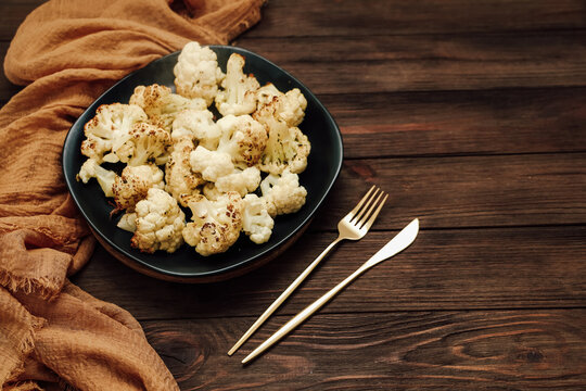 Cauliflower dish served on a black plate with utensils resting beside it on a wooden table