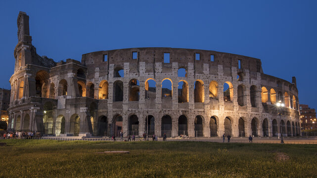 View of the illuminated Colosseum at dusk with ancient stone arches and warm lighting in Roma, Lazio, Italy.