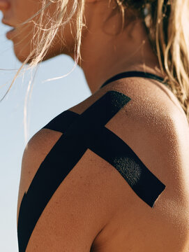 Female athlete shoulder tape side profile black sports tape shoulder muscle outdoor light close up copy space skin texture blonde hair sports therapy