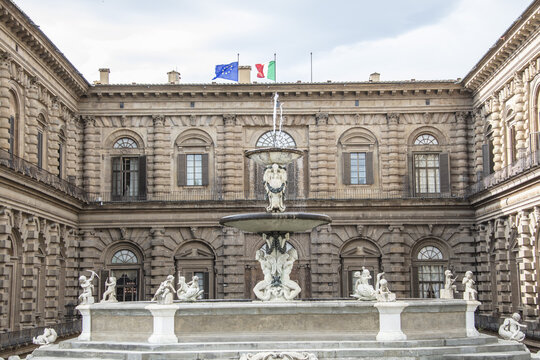 View of the Artichoke Fountain in the courtyard of Palazzo Pitti with ornate stone architecture and flags flying in Florence, Tuscany, Italy.