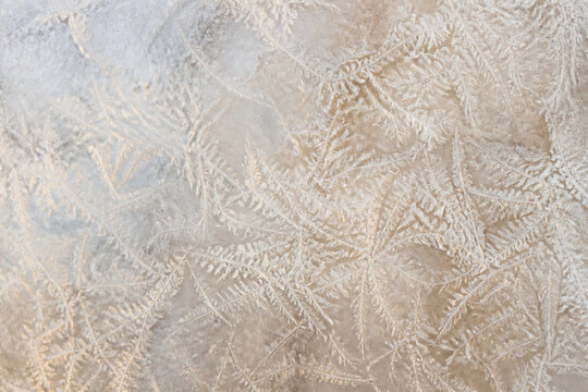 A close-up texture of frost patterns covering a light-colored surface, suggesting a cold outdoor setting.