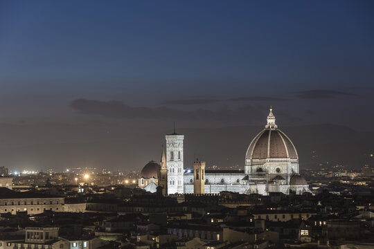 View of the illuminated Cathedral of Santa Maria del Fiore and Giotto's Campanile rising above the historic rooftops of Florence at night in Florence, Tuscany, Italy.