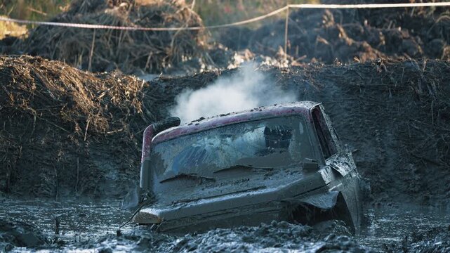 Extreme off road truck stuck in deep mud pit. Red vehicle is almost completely covered in thick brown mud as white smoke rises from engine. Thrilling adventure sport competition concept